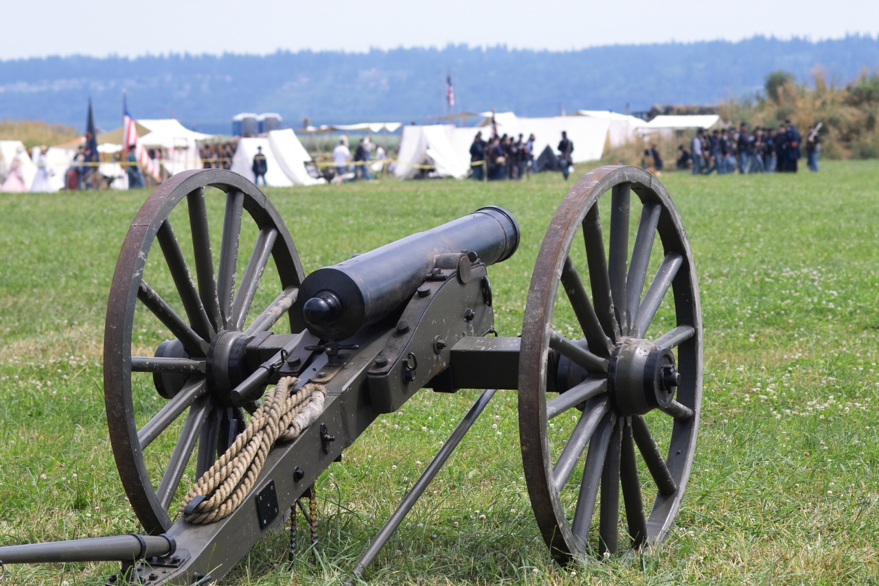 civil war era cannon posed on green grass facing white civil war era tents