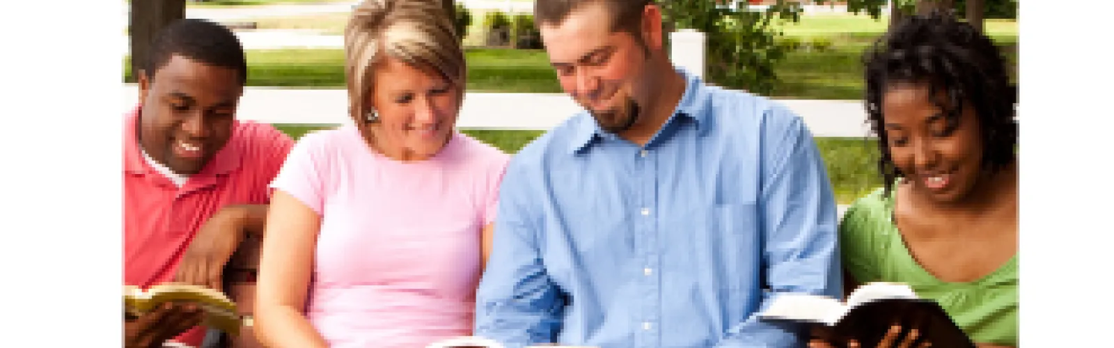 Diverse group of young adults sitting on a park bench reading books together and smiling outdoors